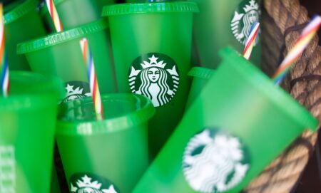 A set of green Starbucks brand cups with red, white, and blue straws in a pile together.