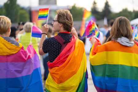 Wrapped in bisexual flag and pride flags this trio are watching a gay pride event