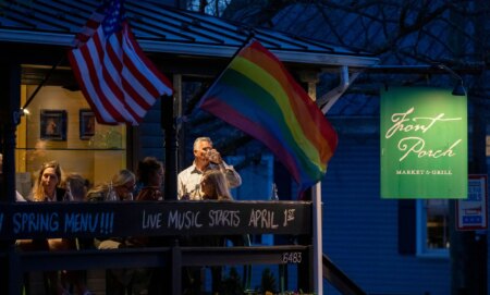 Residents drink on the balcony of a restaurant as the sun goes down, while a Pride and US flag wave.