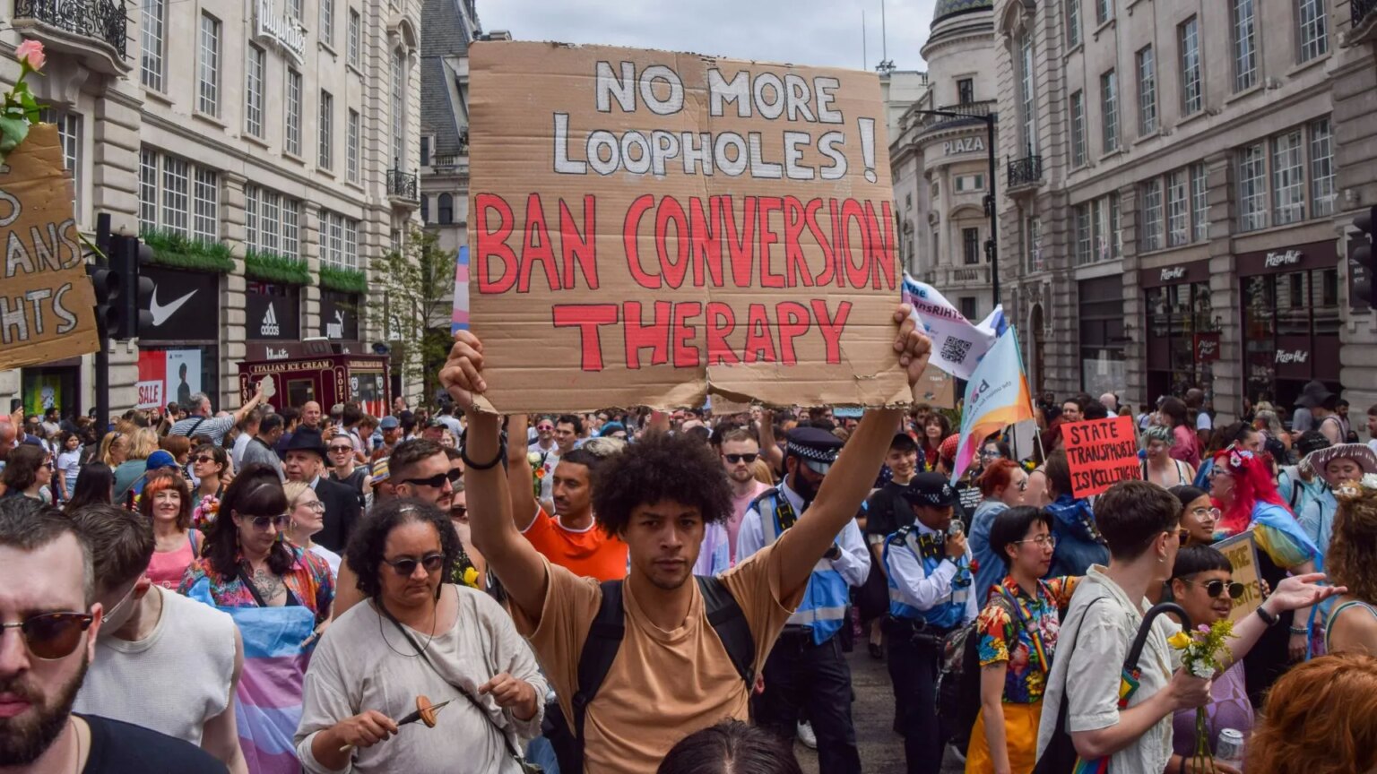 Des députés et des experts critiquent le gouvernement pour le report de l’interdiction de la thérapie de conversion : « un échec moral » Protester in crowd holds up a sign that reads