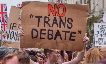 An individual holds up a cardboard sign that reads