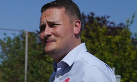 Wes Streeting wears a blue button shirt while walking around outside.