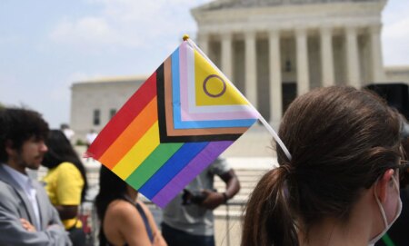 A person standing outside of the US supreme court with an LGBTQ+ flag in their hair.