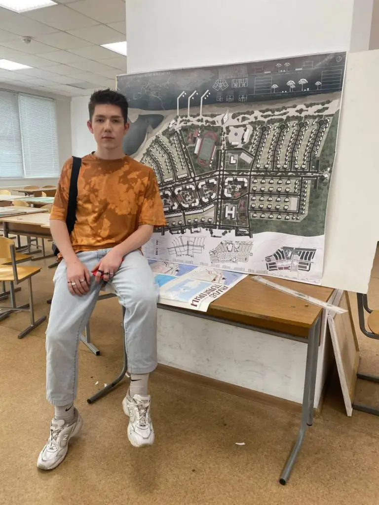 Max, étudiant gay russe, est assis sur une table et pose devant une photo d'une ville