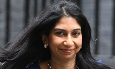 Suella Braverman, smiling as she walks down a walkway.