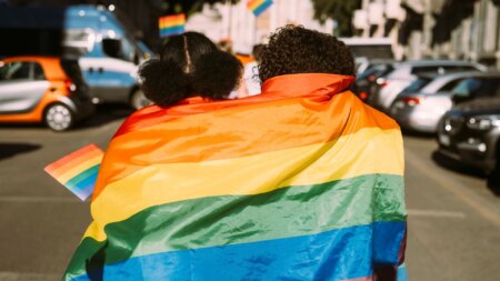 Two people facing backwards wrapped in a Pride flag