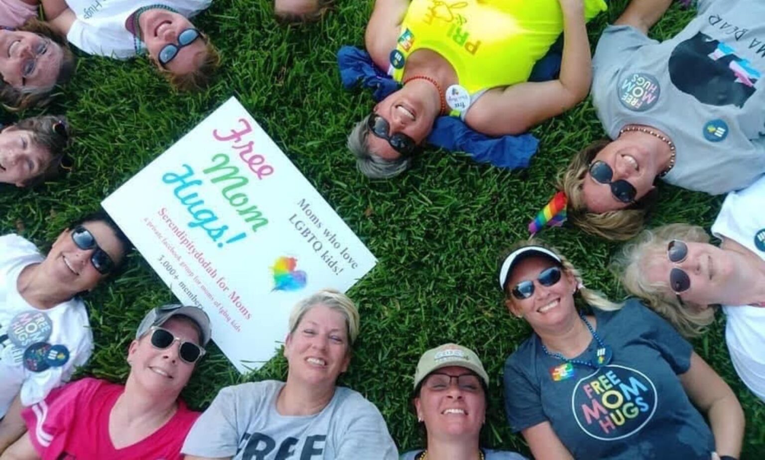 Rencontrez les « Mama Bears » qui ripostent dans les États dirigés par les républicains pour protéger les enfants LGBTQ+ Liz Dyer and a group of moms of LGBTQ+ youth who are part of the Mama Bears group sit on the grass with a 'free hugs' sign