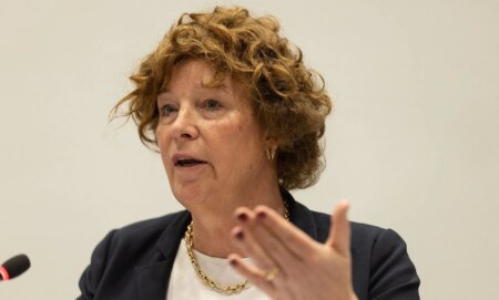 Petra De Sutter speaking into a pedestal microphone whilst gesturing with her hand.