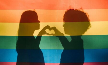 People making a heart shape behind a pride flag