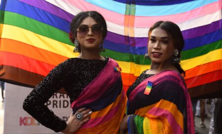 Members of the LGBTQ+ community in India stand infront of a Pride rainbow flag.