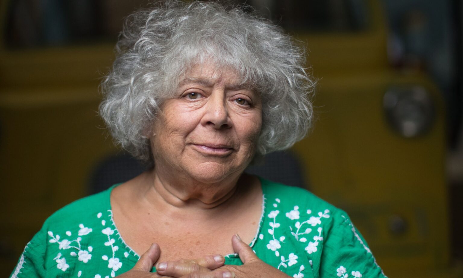 Miriam Margolyes dit que l’acteur trans l’a aidée à changer d’avis sur les pronoms neutres Actor Miriam Margoyles wears a green shirt with while spots on it while her hands cover her chest over her heart