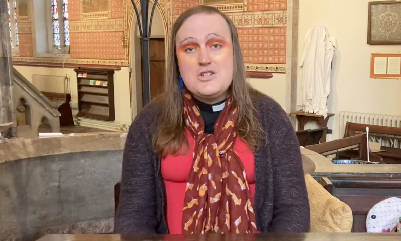 Le premier prêtre non binaire de l’Église d’Angleterre à propos de la découverte de son sexe : « J’étais dans beaucoup de déni » Bingo Allison, a non-binary, genderqueer Church of England priest, wears a red top, sweater and scarf while they speak about religion and Trans Day of Visibility