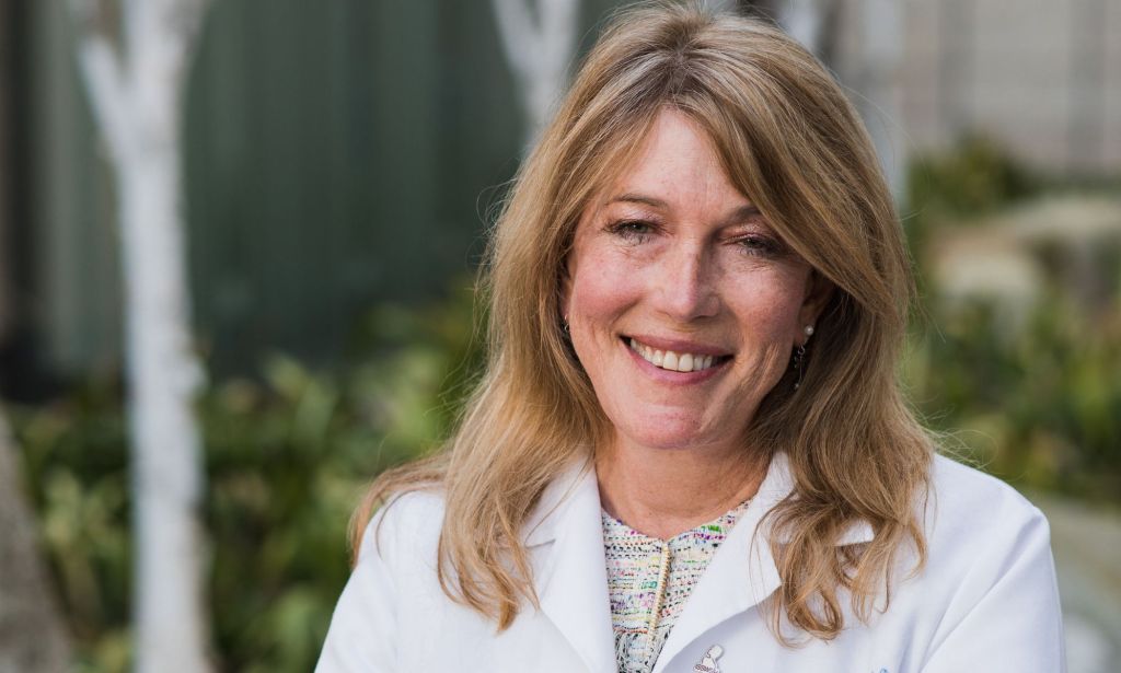 Le Dr Marci Bowers, experte en soins de santé trans, sourit alors qu'elle pose dans une tenue blanche avec une veste chirurgicale blanche à l'extérieur