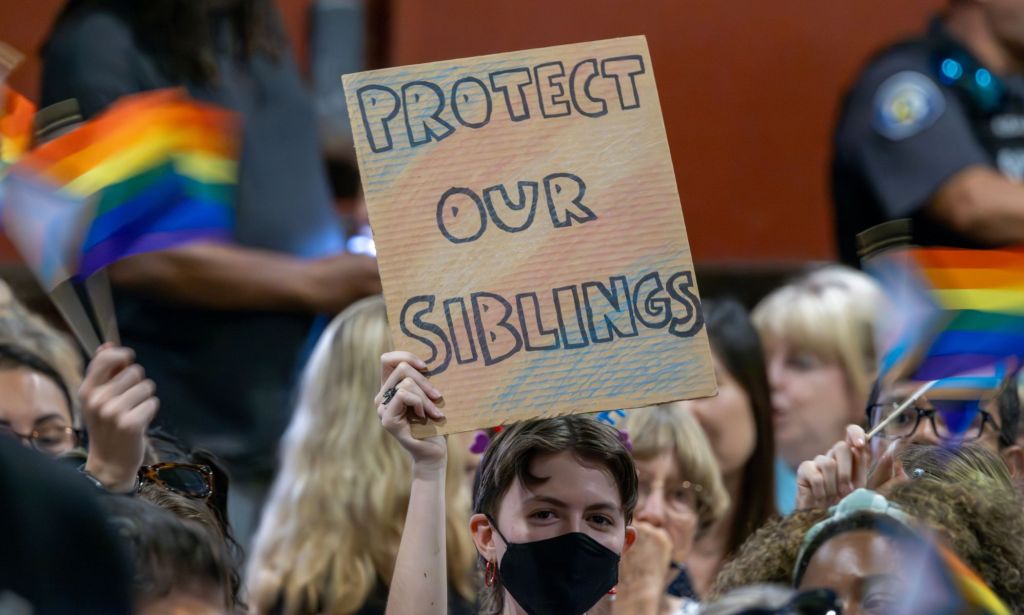 Une personne brandit une pancarte indiquant « Protégez nos frères et sœurs » avec les couleurs du drapeau trans sur la pancarte alors qu'elle proteste contre les politiques anti-trans défendues par des groupes conservateurs et des législateurs, y compris les candidats républicains à la présidentielle de 2024, lors des débats.