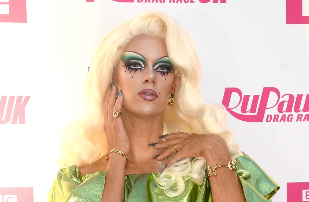 Crystal, candidate de Drag Race UK, pose dans une robe verte sur fond blanc et rose