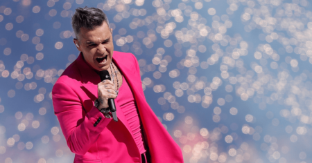 Robbie Williams porte une tenue rose alors qu'il chante dans un micro