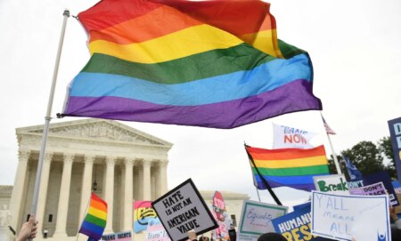 An LGBTQ+ flag waving above a state capitol building.