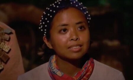 A screenshot from Survivor 41 of contestant Erika Casupanan wearing a light coloured shirt and dark headband with pearls on it