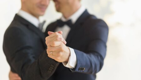 Two grooms clasping hands with a wedding ring visible