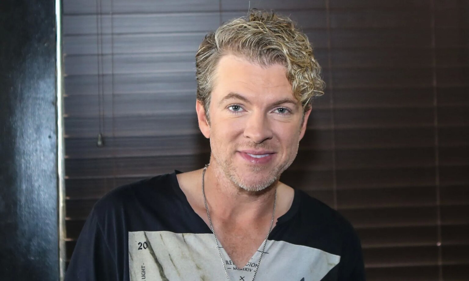 La star de Rascal Flatts obligée de nier la rumeur trans déclenchée par des trolls en ligne Joe Don Rooney smiling in a black and grey top.