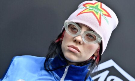 Billie Eilish, who created a song for the Barbie soundtrack, wears a blue jacket, glasses and a pink beanie with a neon star pattern on it