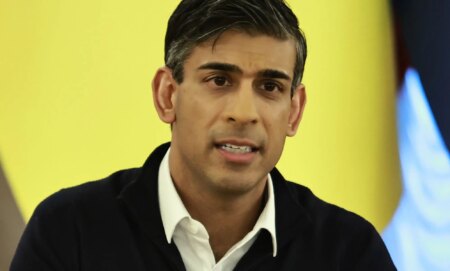 Rishi Sunak, with teeth gritted, infront of a yellow flag.