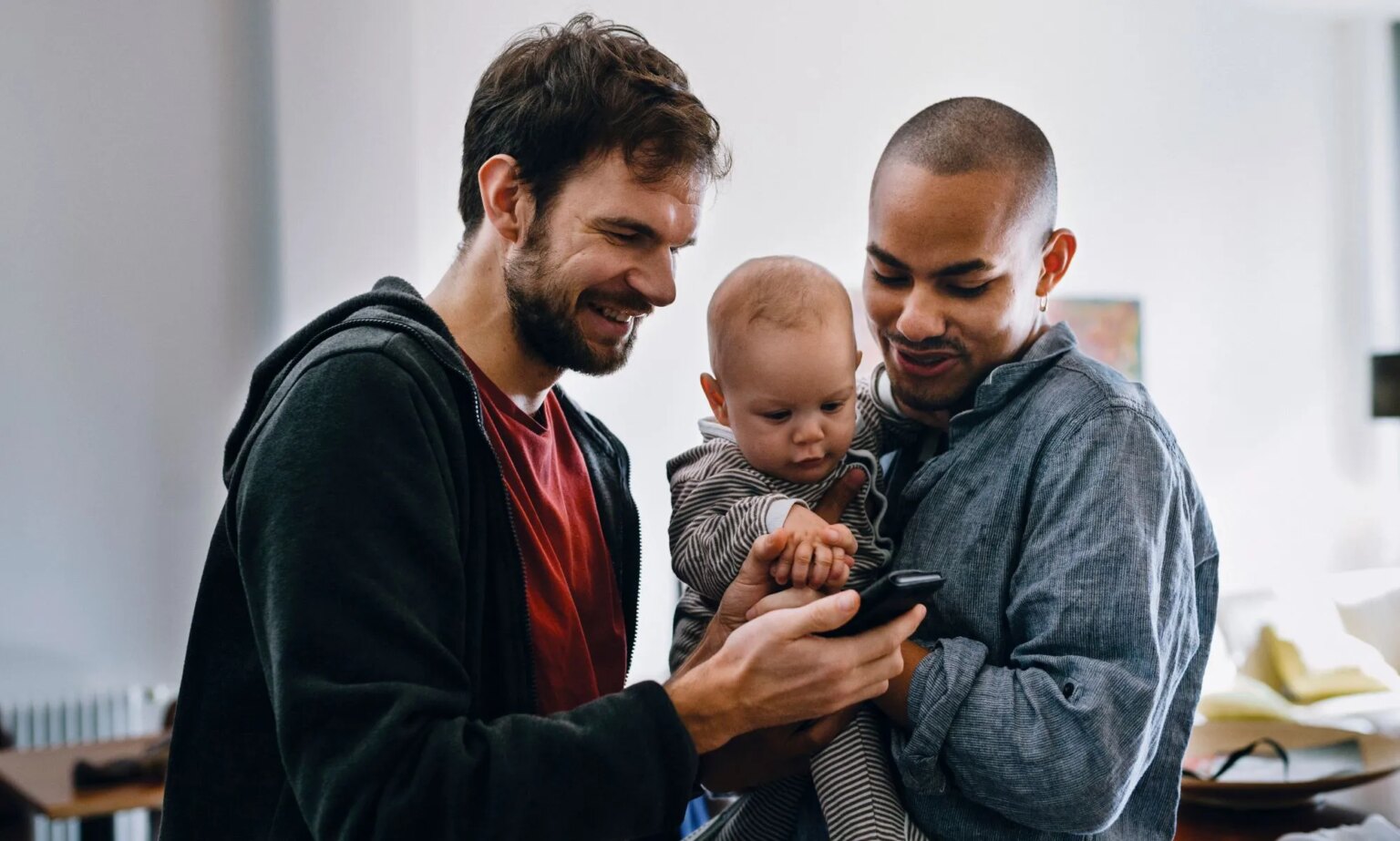 La discrimination en matière d’adoption « retient » les familles LGBTQ+ potentielles aux États-Unis Two men holding a baby watch a video on their mobile phone.