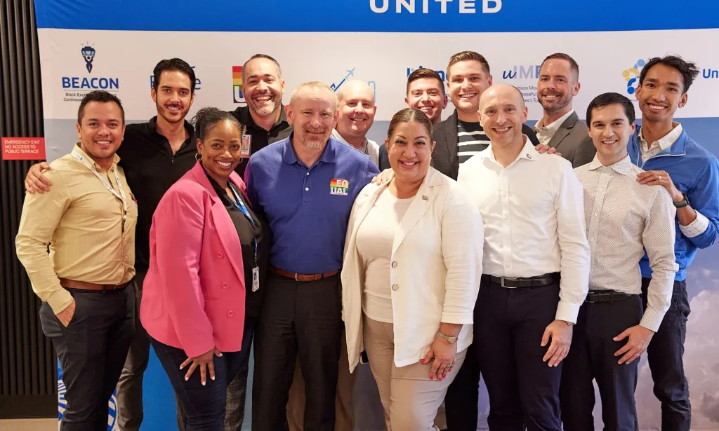 Il s’agit d’une image d’un groupe diversifié de personnes debout devant un panneau d’United Airlines. 