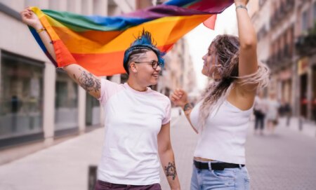 two women holding a pride flag and looking at each other romantically