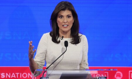 Nikki Haley, who is the top rival to Donald Trump in the 2024 Republican presidential nominee race, wears a white outfit as she speaks into a microphone attached to a podium