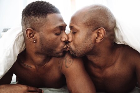 Two Black men in bed kissing under a duvet