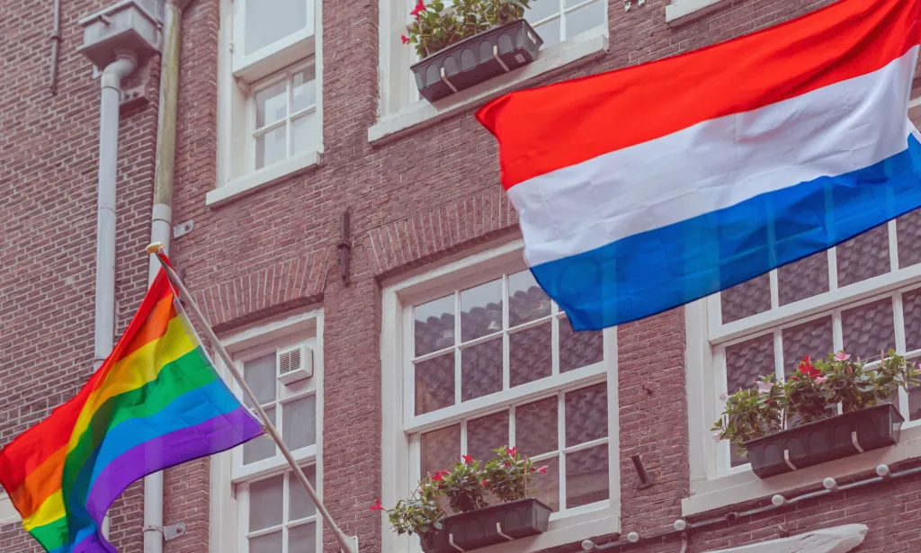 Il s'agit d'une image du drapeau de la fierté flottant à côté du drapeau des Pays-Bas sur un bâtiment à Amsterdam. 