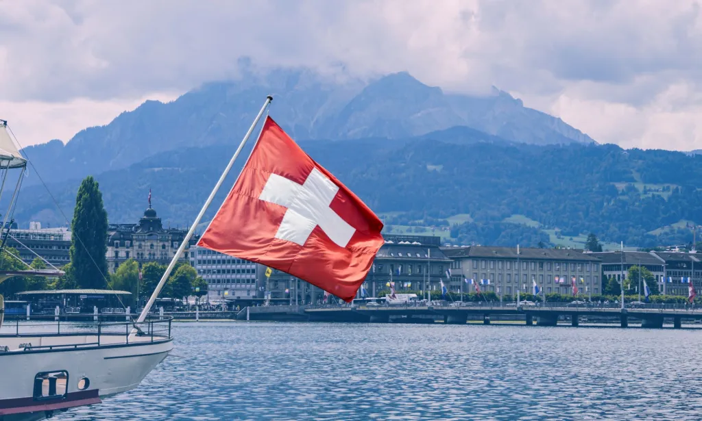 Il s'agit d'une image du drapeau suisse à l'arrière d'un bateau.  En arrière-plan, il y a une montagne.