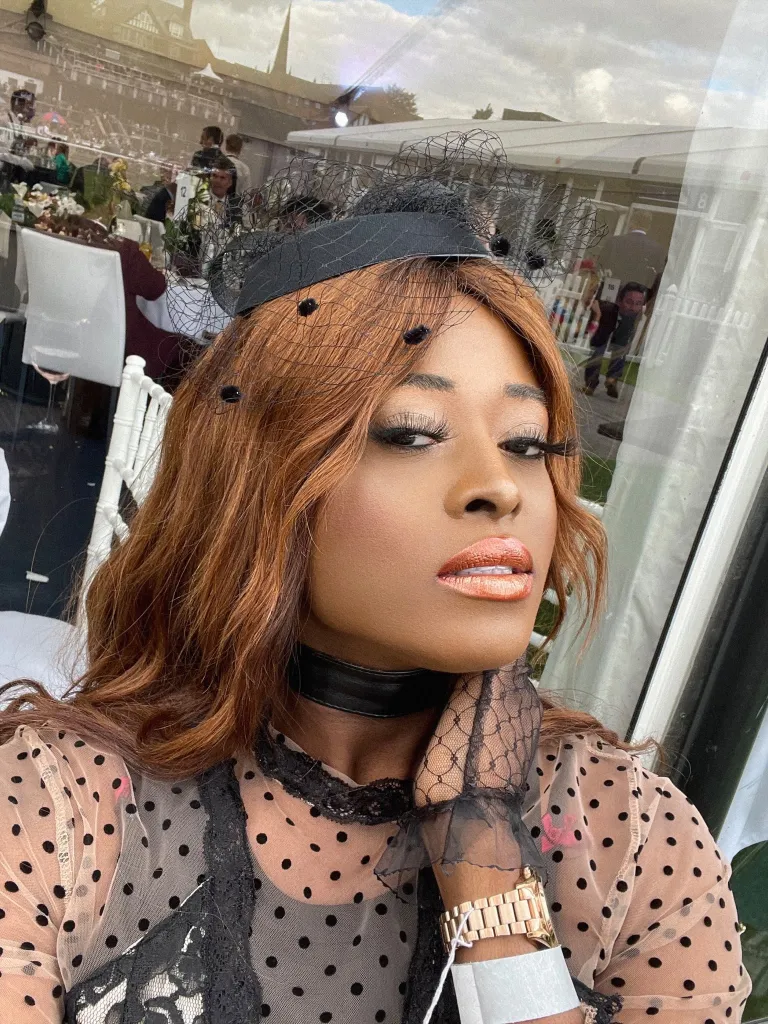 Il s'agit d'une image d'une femme trans noire nommée Robyn Electra.  Elle porte une élégante robe noire et un fascinator noir.