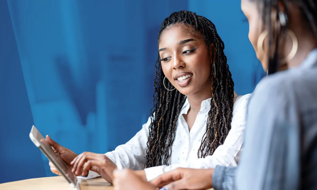 Il s'agit d'une image de 2 femmes noires au travail.  Ils regardent tous les deux une tablette.