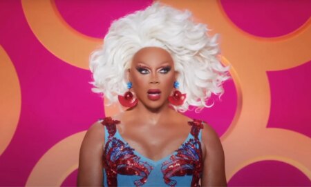 A screenshot of RuPaul watching a lip-sync during All Stars 8. She is wearing a red and blue dress and looks shocked.