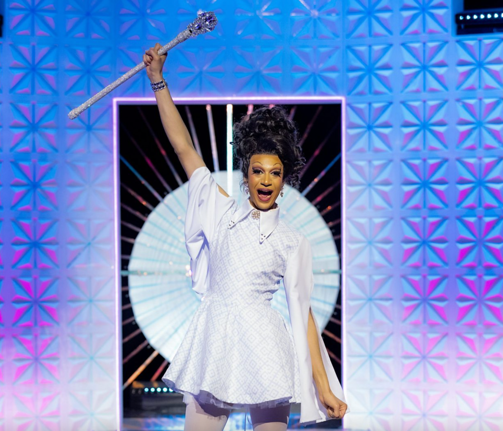Tia Kofi, gagnante de la deuxième saison de Drag Race UK vs The World, tient son sceptre en l'air.