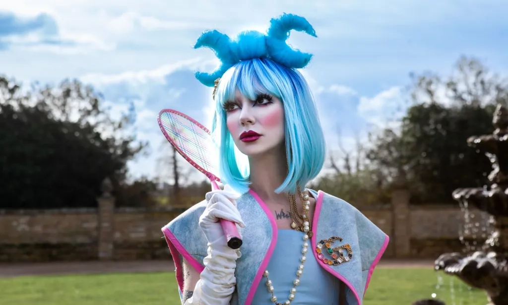 Bambie Thug dans une perruque bleue tenant une raquette de tennis rose.