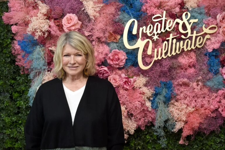 Marsha Stewart in front of a multicoloured floral display that, to be honest, we chose as it kind of looked like the colours of the trans flag.