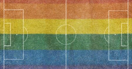 Vue aérienne d'un terrain de football en herbe sans personne et avec des lignes blanches peintes, avec le drapeau arc-en-ciel lgtb peint sur l'herbe.