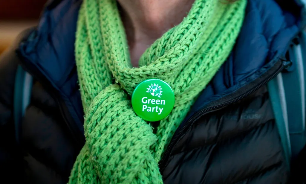 Un membre du Parti Vert portant un foulard et un insigne du Parti Vert.