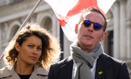and Laurence Fox are standing together with an England flag blowing behind them
