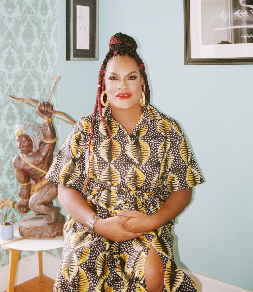 Il s'agit d'une image d'une femme trans noire.  Elle porte une robe colorée et a les cheveux tressés. 