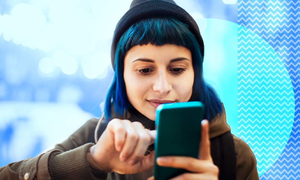Une femme aux cheveux bleus et au bonnet regarde son téléphone.