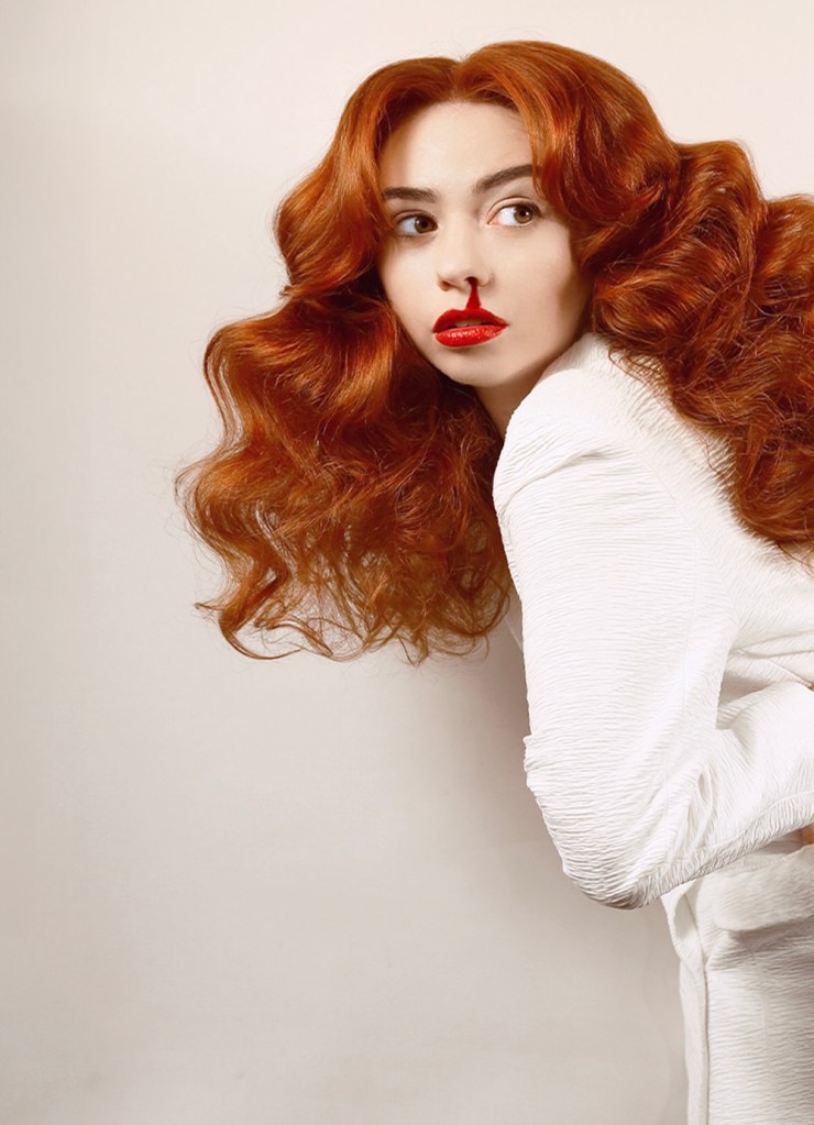 Hannah Platt : Mécanisme de défense. Hannah avec de grands cheveux roux portant une robe blanche. Son saignement de nez se mélange avec le rouge à lèvres rouge
