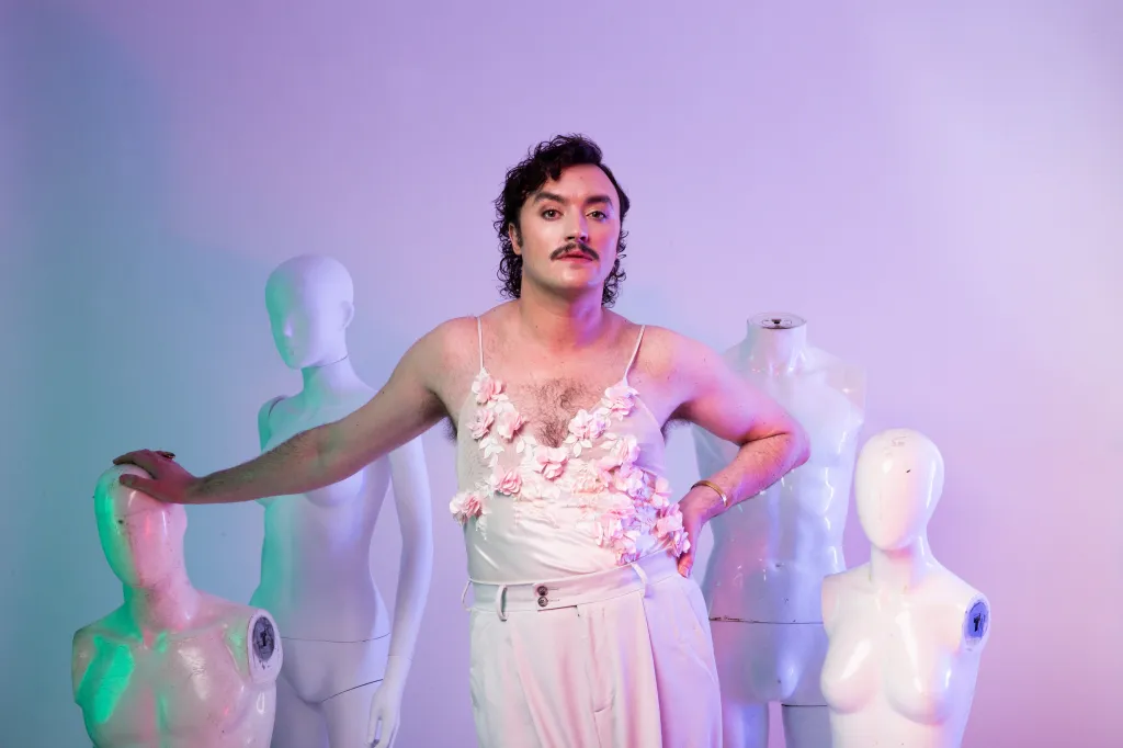 Dan Wye : Dan Wye Am I Sam Smith ? au Fringe d'Édimbourg. Dan porte un haut à bretelles et un pantalon roses, ils s'appuient sur l'un des quatre mannequins blancs sans bras ni tête.