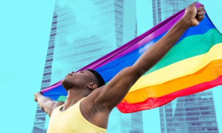 This is an image of a Black man holding a Pride flag in front of an office building