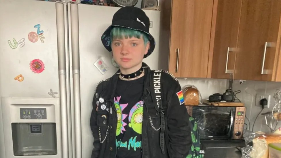 Les parents d'un adolescent qui s'est suicidé demandent plus de soutien pour les transgenres de moins de 18 ans Jason Pulman, seen here wearing a hat. He has blue hair and is wearing a backpack and largely black clothing.