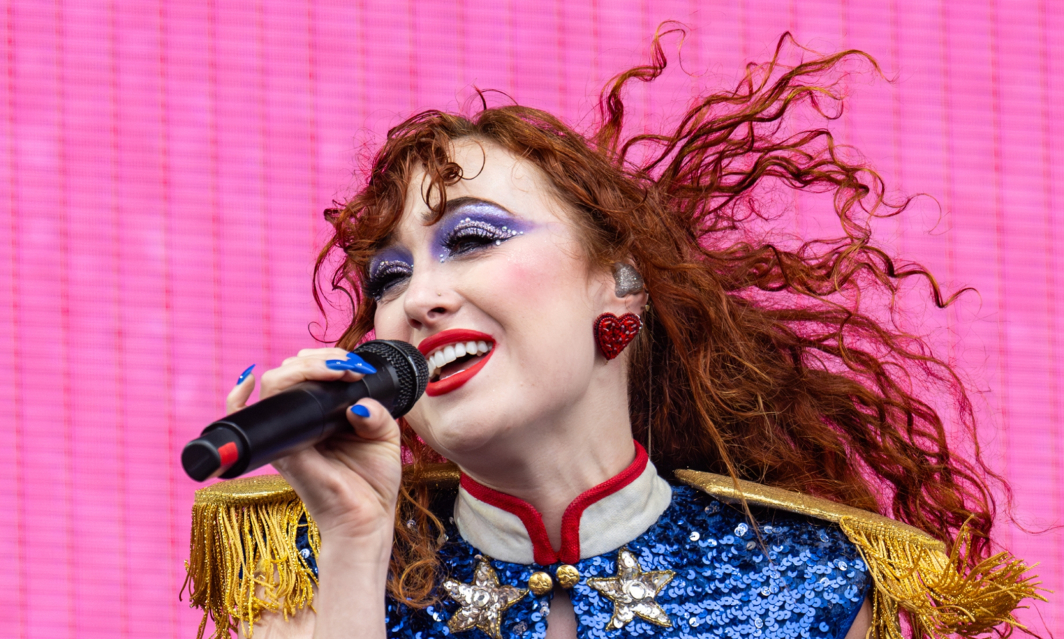 La signification LGBTQ+ « secrète » derrière le bop saphique emblématique de Chappell Roan Pink Pony Club Chappell Roan performing against a bright pink background. She is wearing a blue sequin and gold fringe shirt with big red earrings