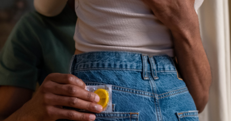 Couple enlacé, l'un d'eux tenant un préservatif.